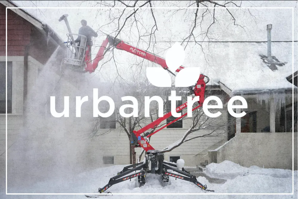 Urbantree workers are trained for professional ice dam removal, utilizing a red boom lift and steam equipment to clear dangerous ice buildup from a snowy home's roof in Minneapolis, MN.