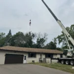 Arborist hanging from the crane line above a Blaine backyard during crane tree removal