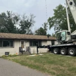 Crane truck set up beside a Blaine home for crane tree removal with the lifting line extended overhead