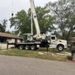 Wide view of a crane truck staged along the street for crane tree removal at a Blaine home