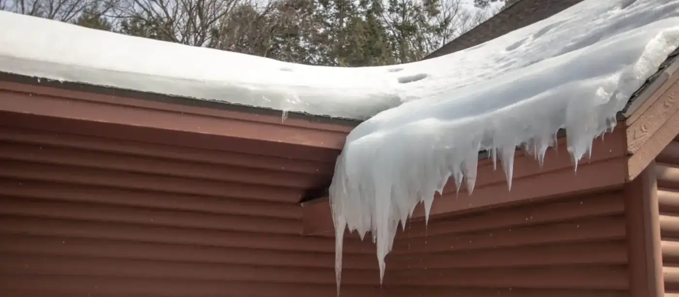 Ice packed solid along a roof eave with snow still lying on the slope above it