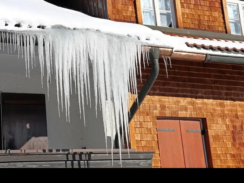 A curtain of icicles hanging from a roof edge above a doorway, with snow banked on the roof behind them