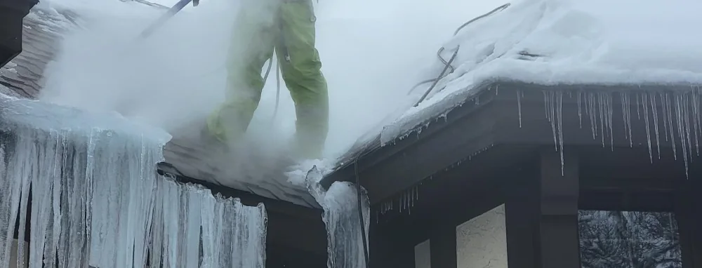 Low-pressure steam lifting an ice dam off a Twin Cities eave, with the icicle curtain still hanging below it