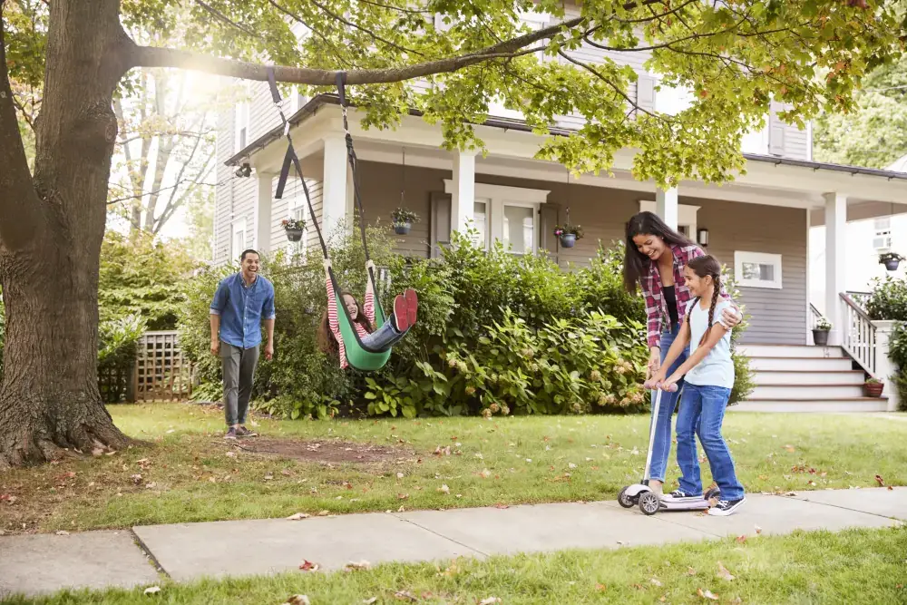 Family playing in a front yard under a healthy mature shade tree with a rope swing, the result of tree work done and cleaned up